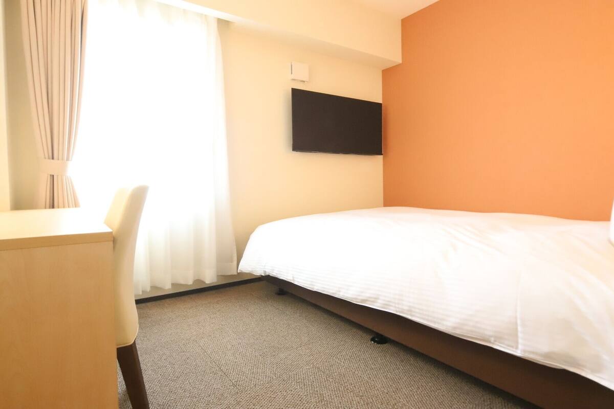 Ein Hotelzimmer mit einem Bett, einem Schreibtisch und einem an der Wand befestigten Fernseher.