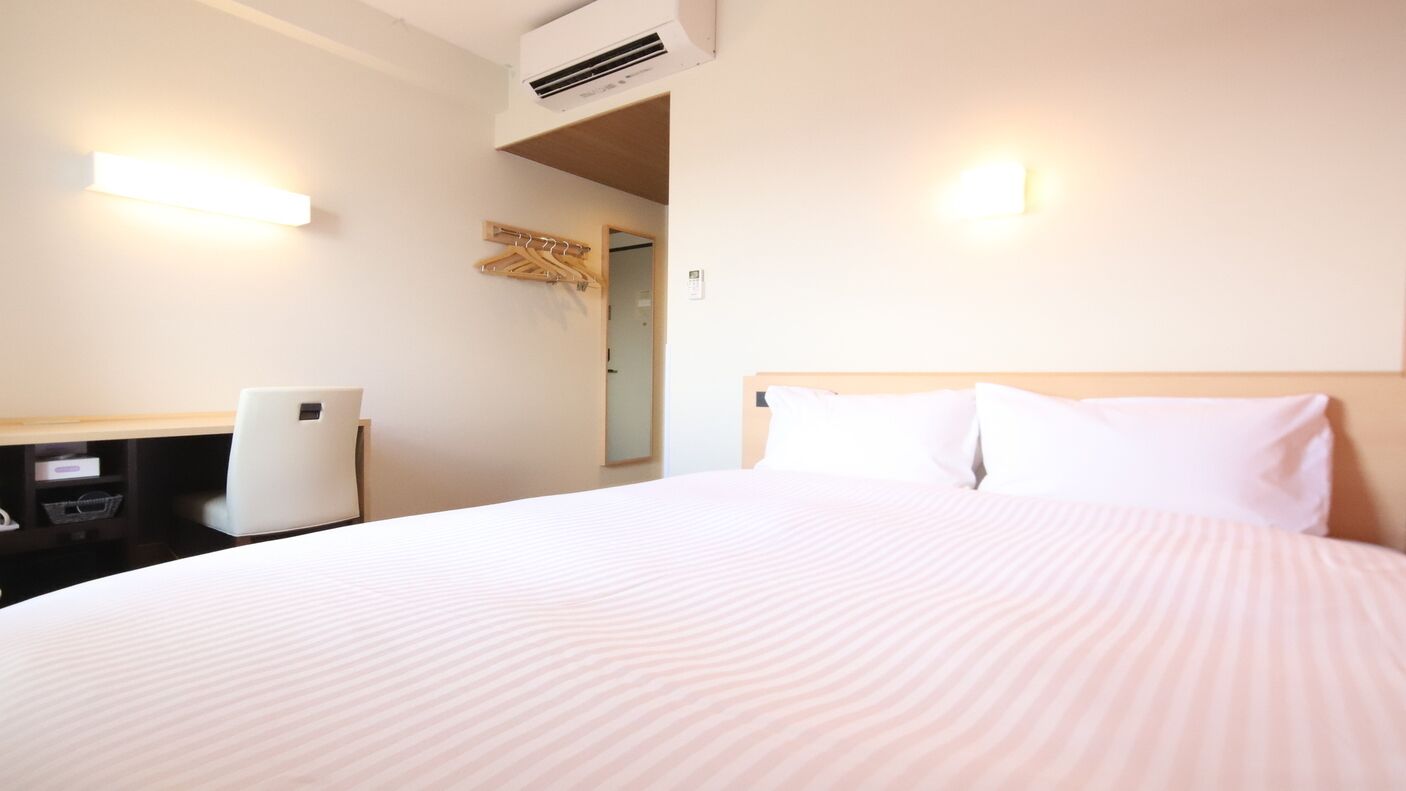 Habitación de hotel con cama, escritorio, silla, aire acondicionado y lámpara de pared.