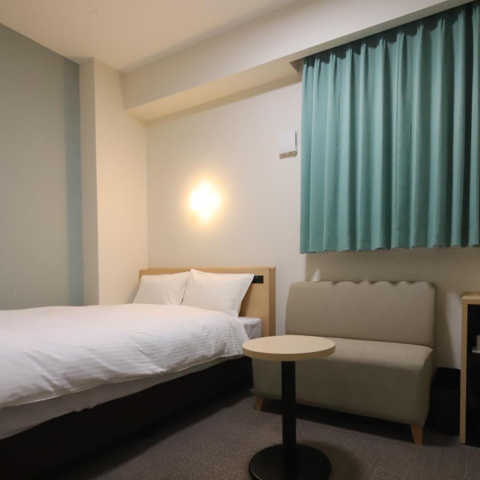 A hotel room with a bed, a small round table, a sofa, and a wall-mounted light.