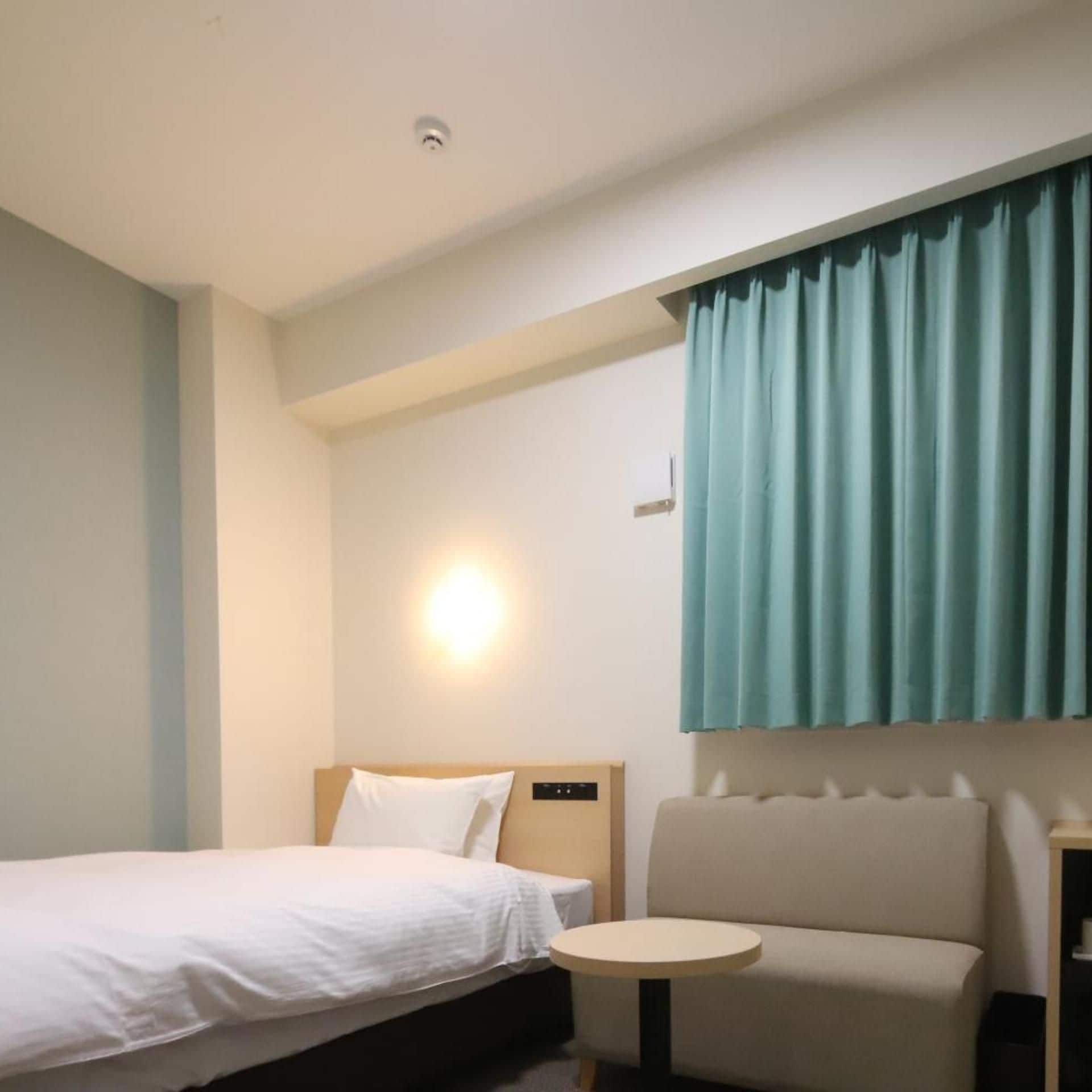 A hotel room with a bed, a small round table, a sofa, and a wall-mounted light.
