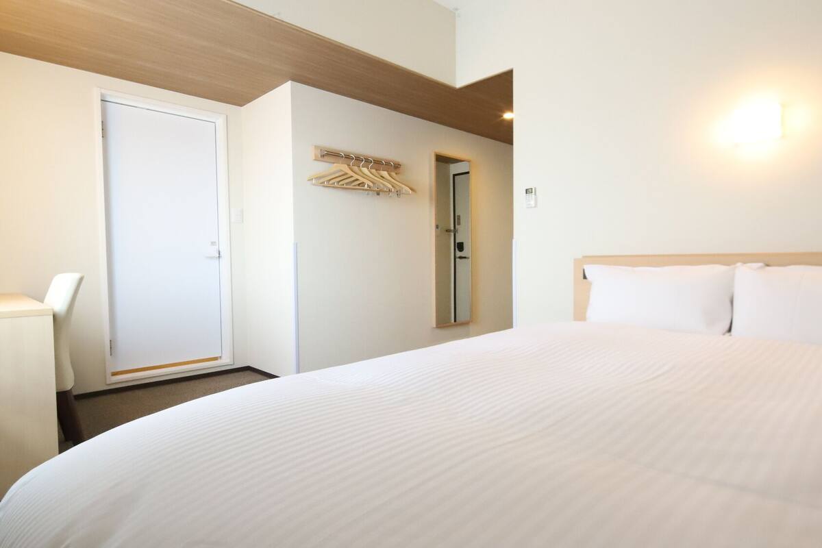 Ein Hotelzimmer mit Bett, Stuhl, Kleiderhaken und einer Tür.