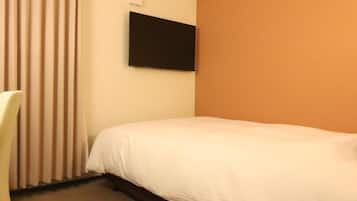 A hotel room with a bed, a chair, a flat-screen TV mounted on the wall, and a carpeted floor.