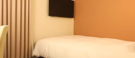 Une chambre d’hôtel avec un lit, une chaise, un téléviseur à écran plat fixé au mur et un sol recouvert de moquette.