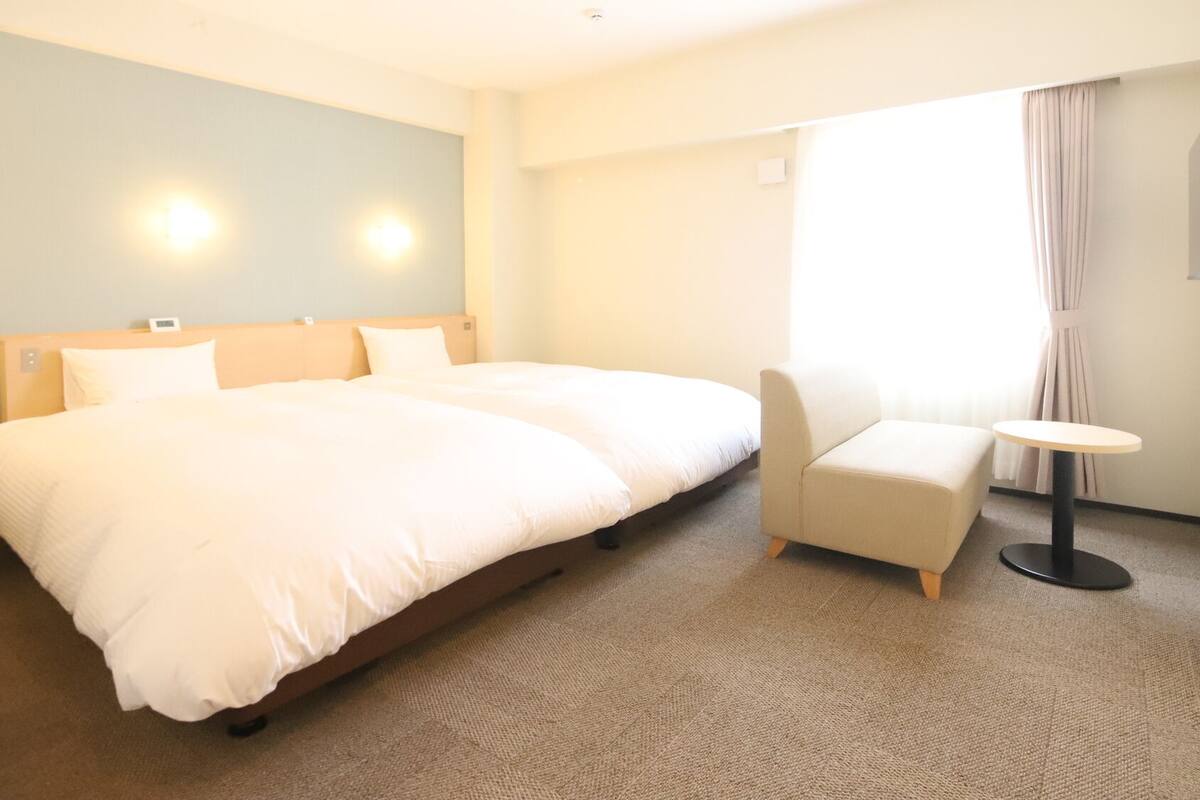 Ein Hotelzimmer mit einem großen Bett, einem Sessel, einem kleinen Tisch und einem Fenster mit Vorhängen.