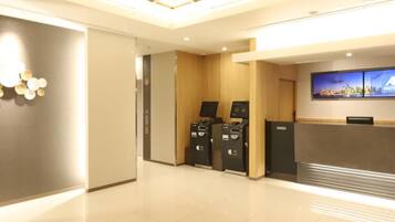 Un espace d’accueil d’hôtel au design moderne, comprenant un comptoir d’accueil, un écran numérique et un kiosque en libre-service.