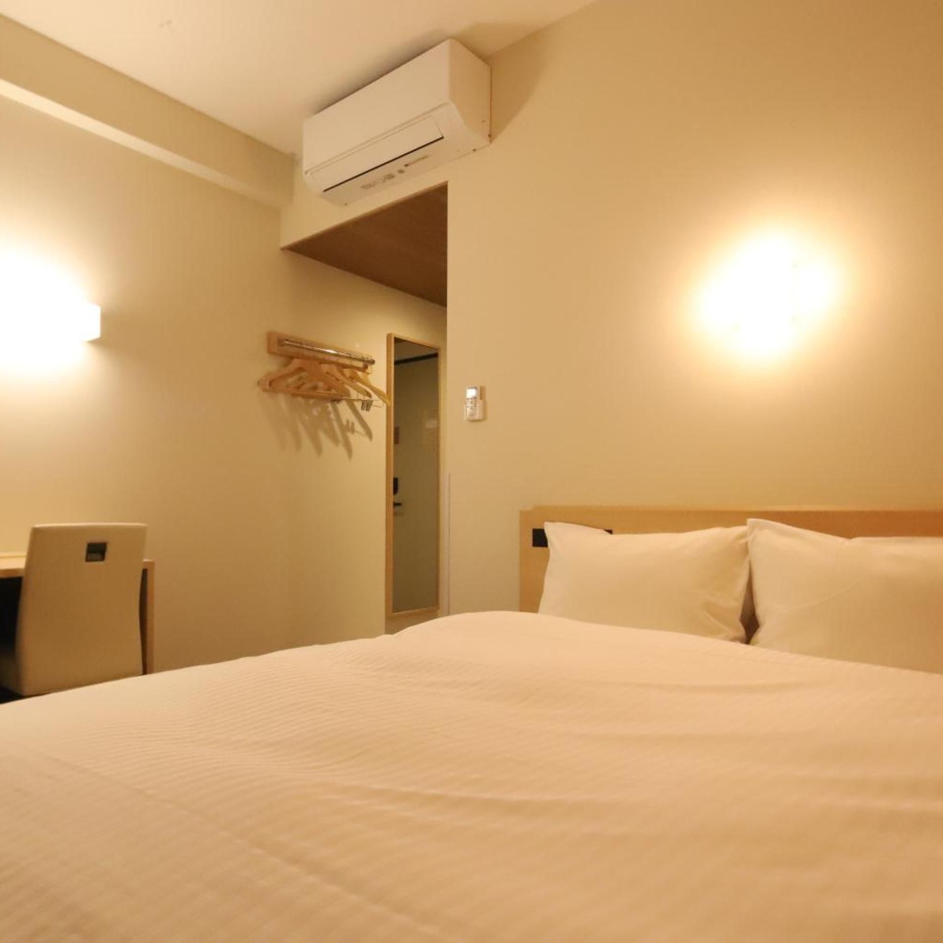 A hotel room with a bed, a desk, and an air conditioning unit.