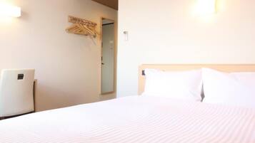 Quarto de hotel com cama, ar condicionado fixado na parede, cabideiro e porta que dá para outro cômodo.