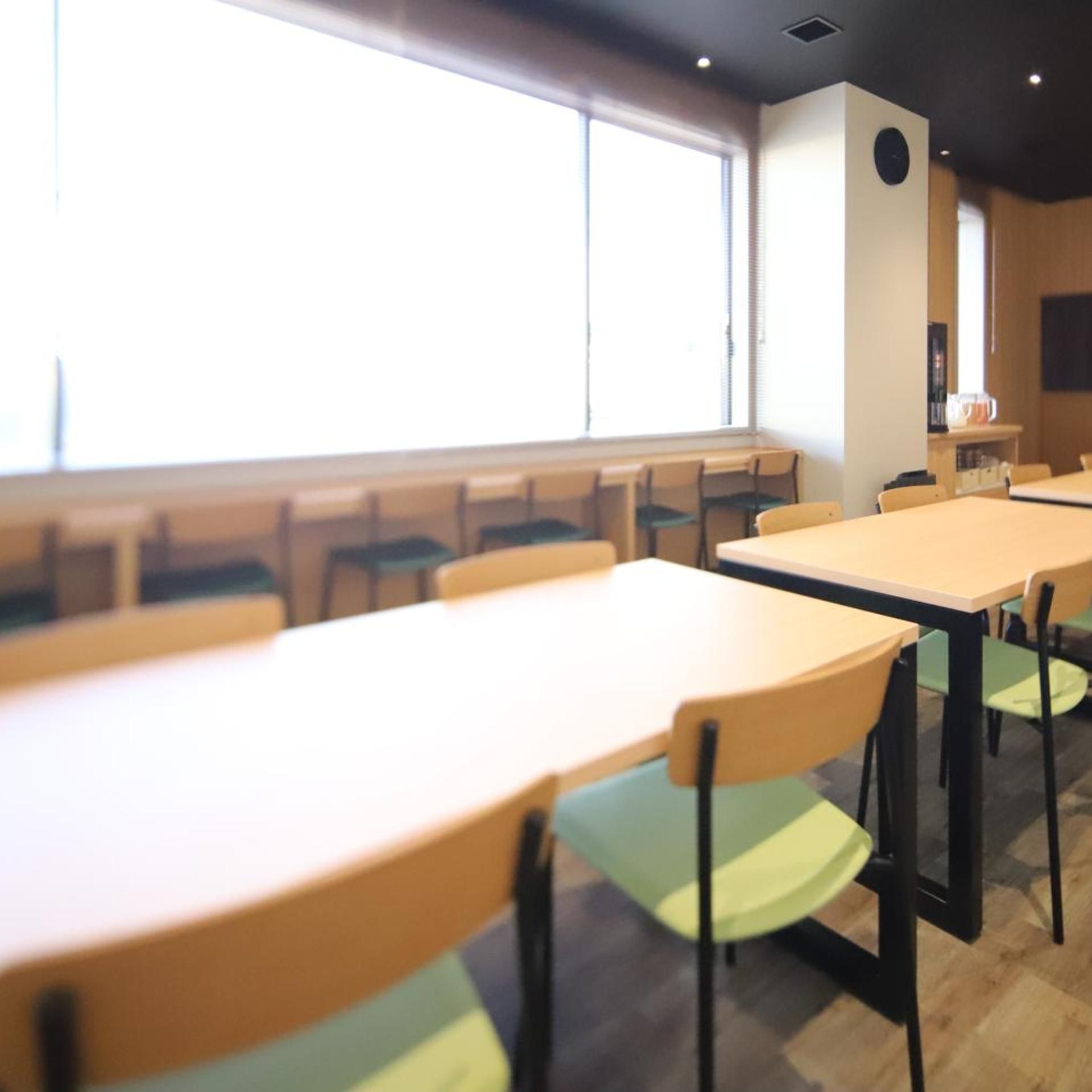 A dining area with tables and chairs, large windows, and a wall-mounted clock.