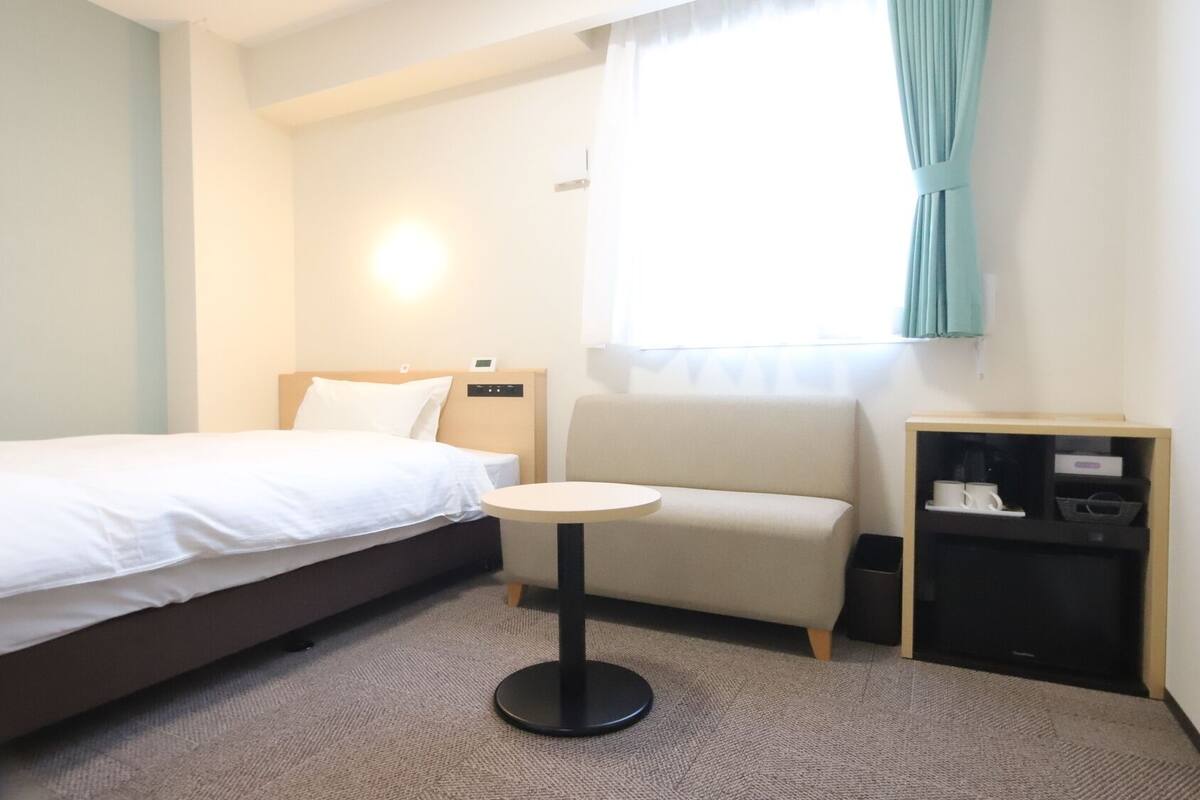 Ein Hotelzimmer mit Bett, einem kleinen runden Tisch, einer Couch und einem Fernseher mit Fernbedienung.