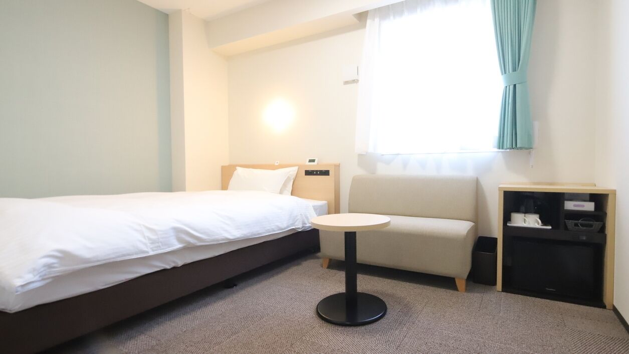 Una habitación de hotel con una cama, una pequeña mesa redonda, un sofá y un mueble para televisión.