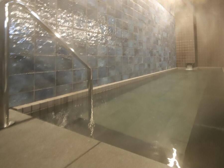 A swimming pool with clear water, a tiled wall, and a metal ladder.