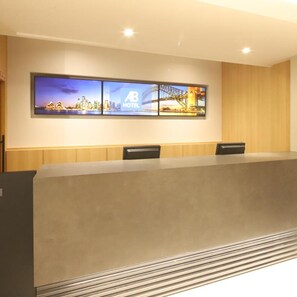 Ett konferensrum med ett långt bord, två stolar och en väggmonterad skärm som visar en stadsbild och hotellets logotyp.