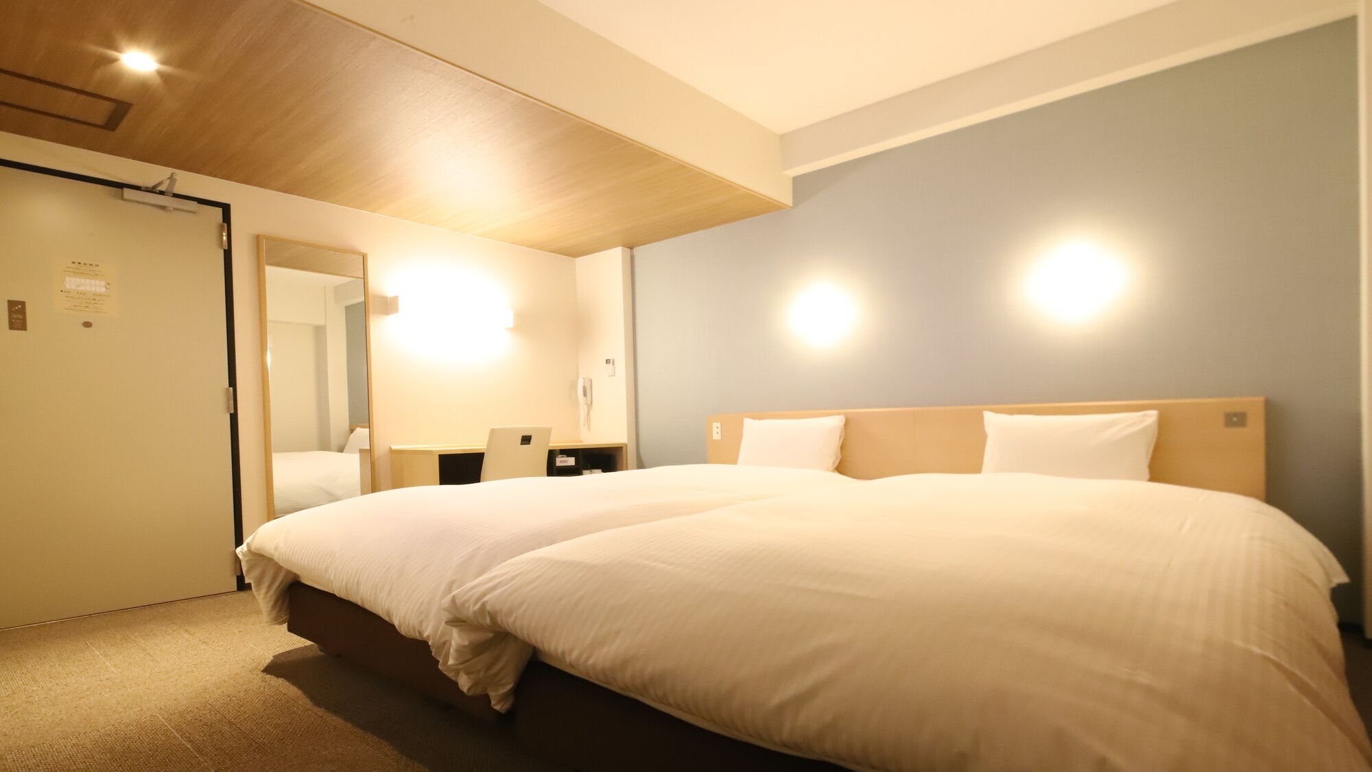 A hotel room with a large bed, bedside tables, a mirror, and a door.