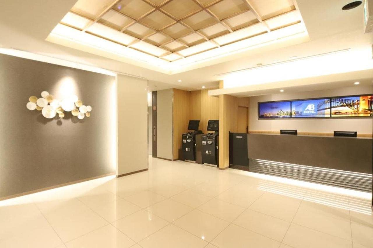 A hotel reception area with a modern design, including a reception desk, a digital display, and a ceiling with a geometric pattern.