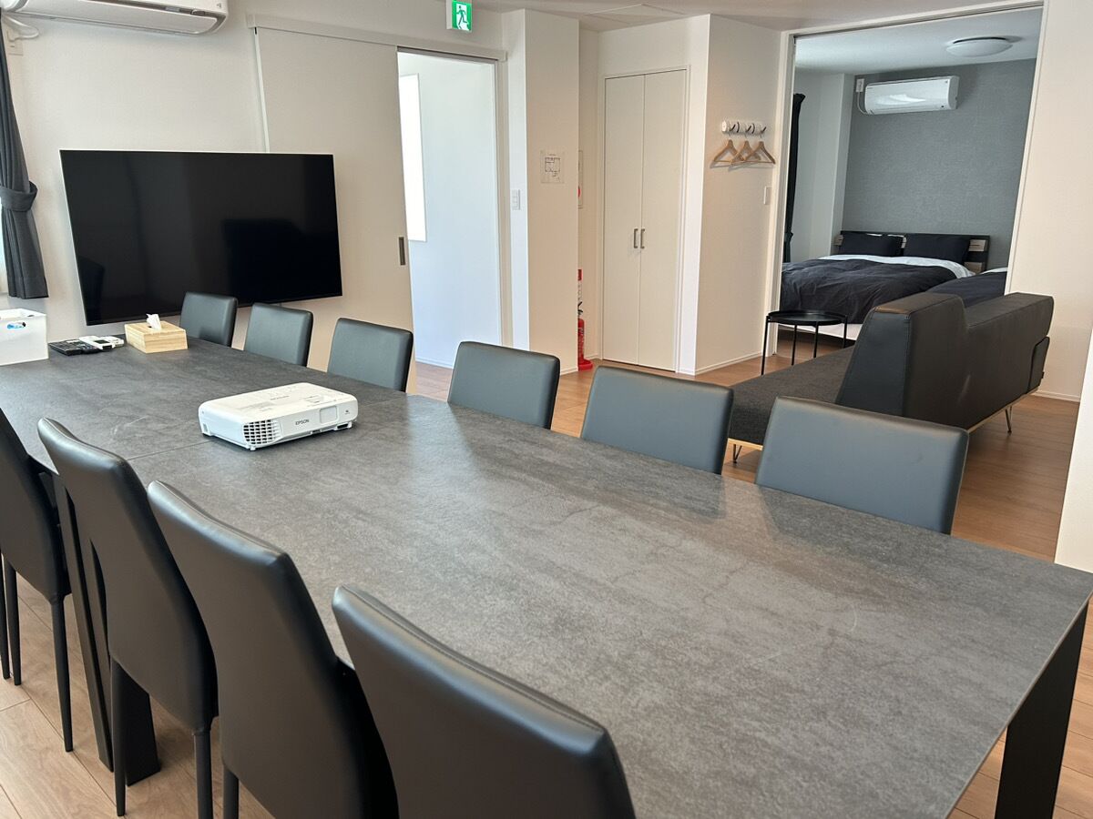 Una sala de conferències amb una taula llarga, cadires, un projector i una pantalla de televisió.