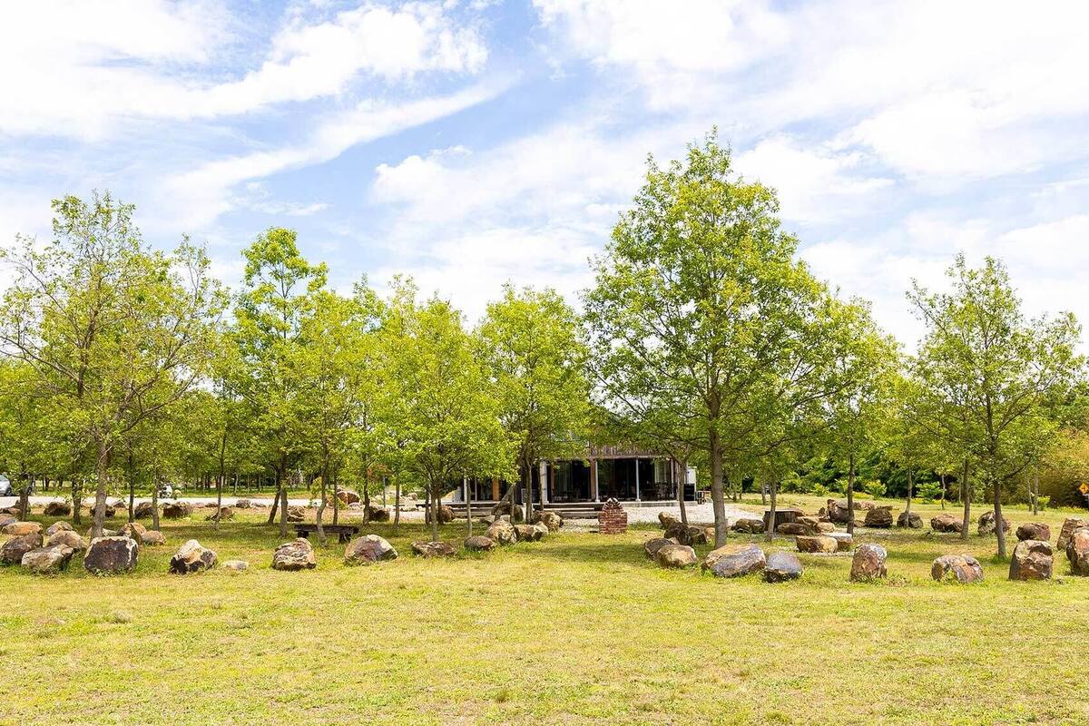 A park with trees, rocks, and a building with a porch.