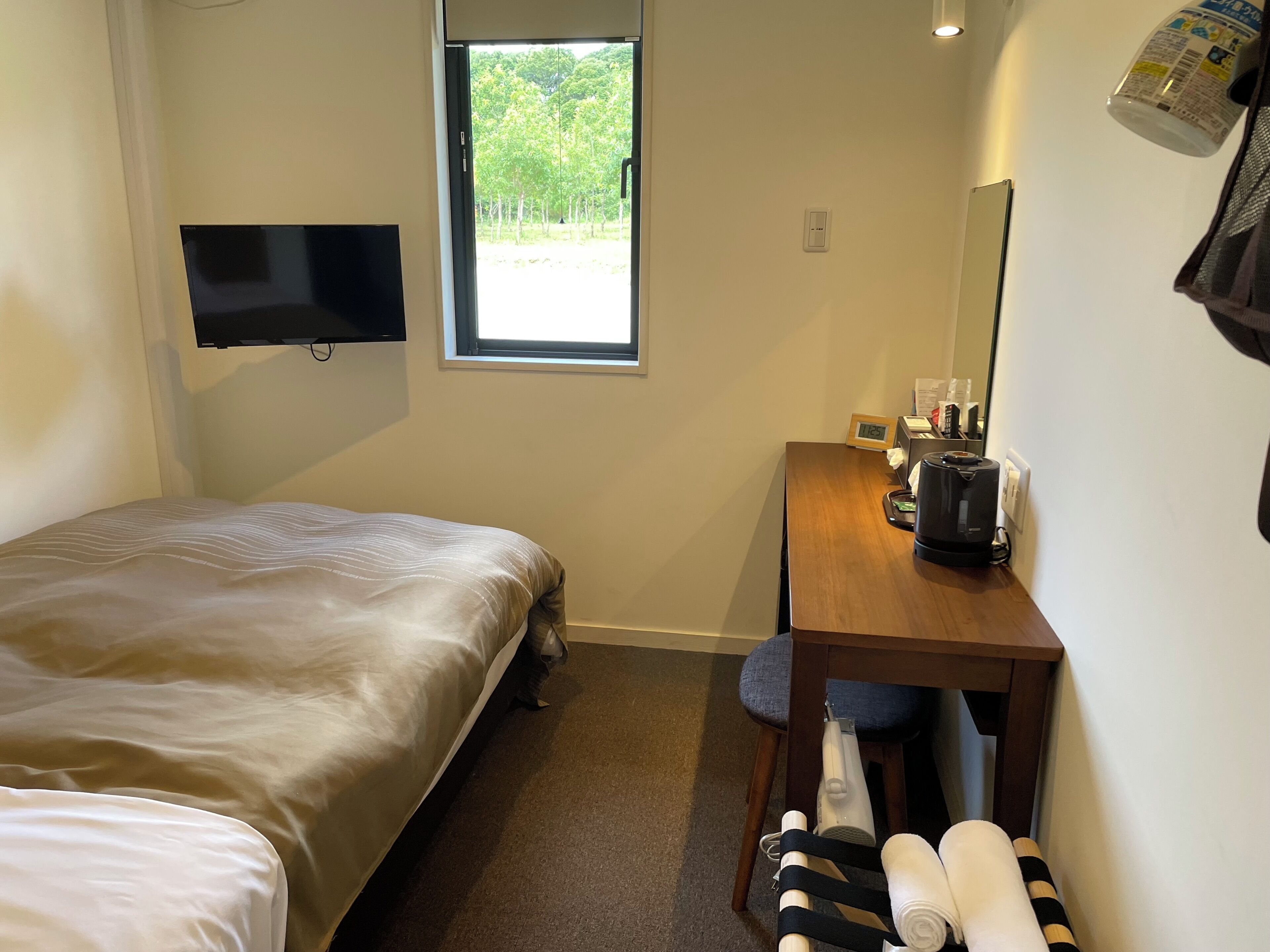 Una habitación de hotel con cama, escritorio con cafetera, televisión, ventana y espejo.