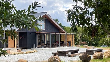 Un edificio moderno con un área de estar cubierta al aire libre, un ventanal grande y un patio de grava con rocas.