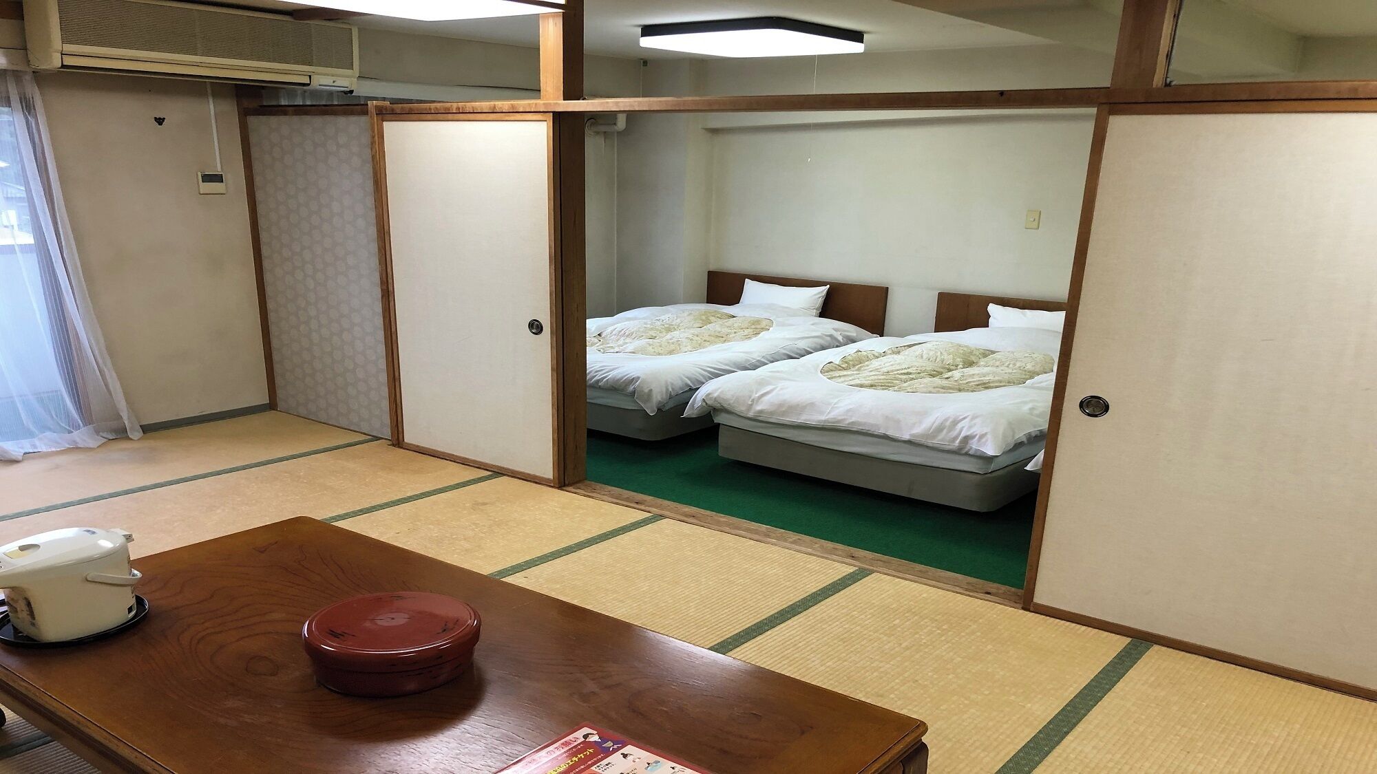 Une pièce de style japonais traditionnel, avec un sol recouvert de tatamis, deux lits, une table en bois et un futon.