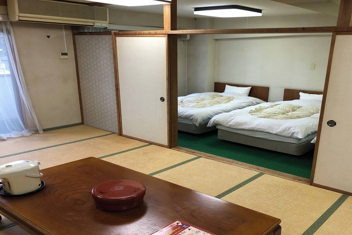 Een traditionele Japanse kamer met tatami vloeren, twee bedden, een houten tafel en een futon.