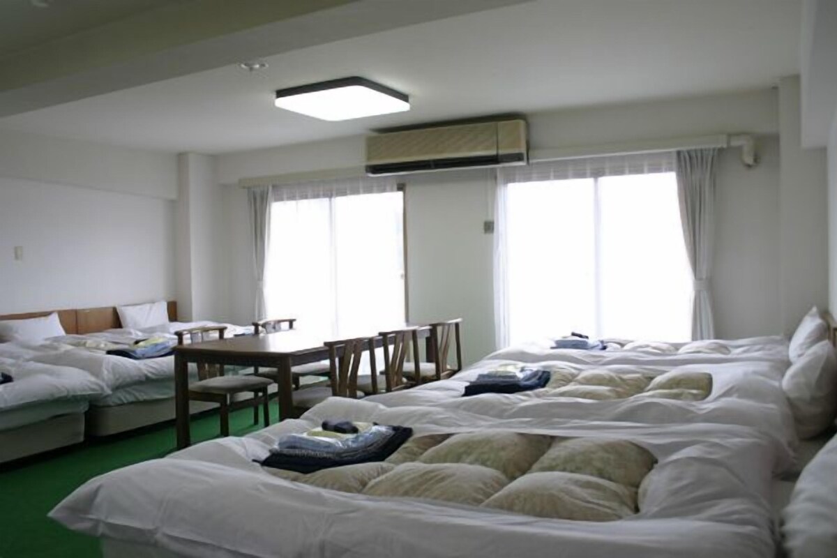 Ein Hotelzimmer mit zwei Betten, einem Esstisch und einem fensterbepflanzten Fenster.