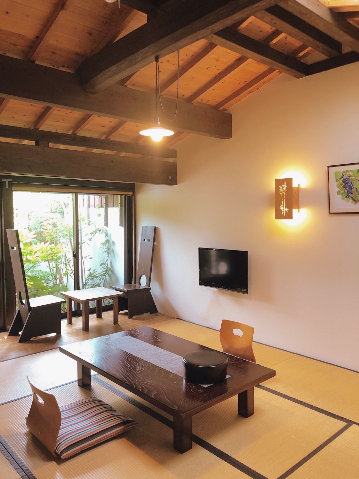 Um quarto japonês tradicional com piso de tatame, uma mesa baixa, uma cadeira, uma televisão e um luminário fixado na parede.
