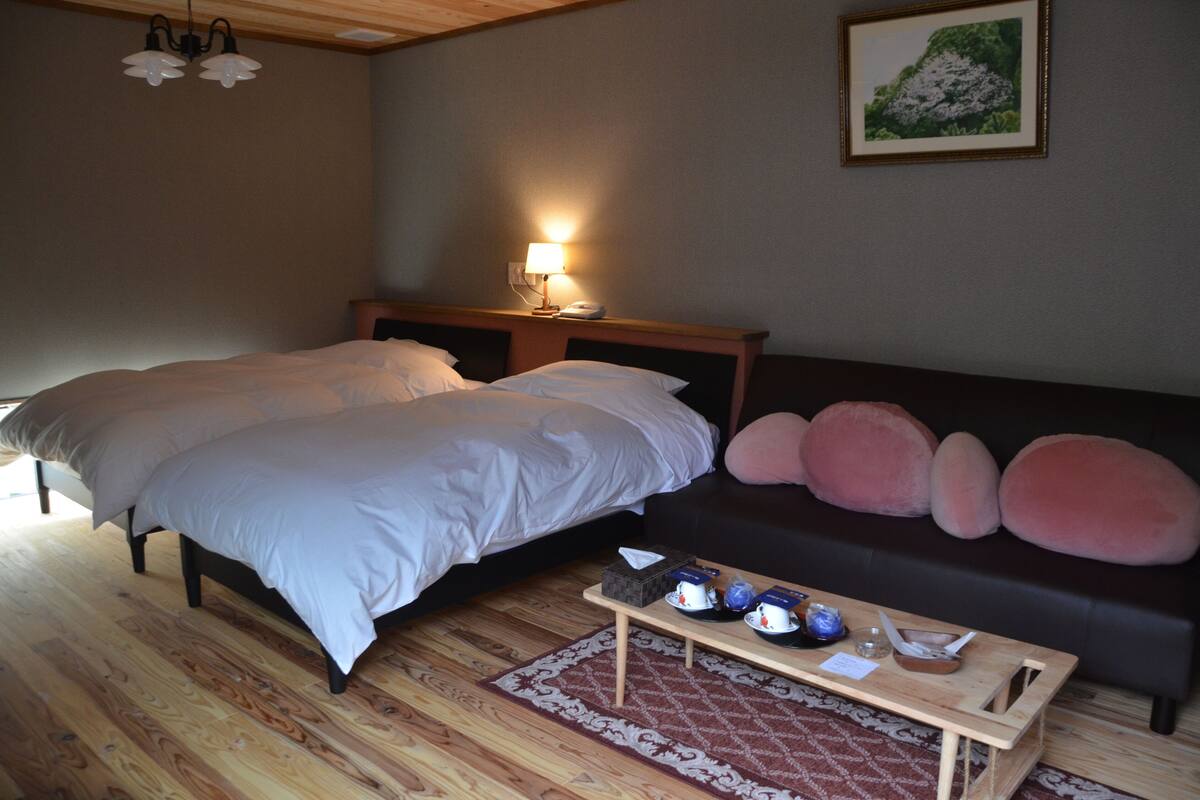 Un dormitorio con cama, mesita de noche, lámpara y un sofá decorado con cojines.