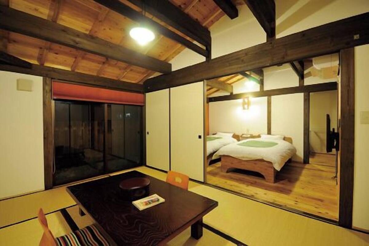 Una habitación tradicional japonesa con suelo de tatami, una mesa de madera baja y una cama con un almohadón verde.