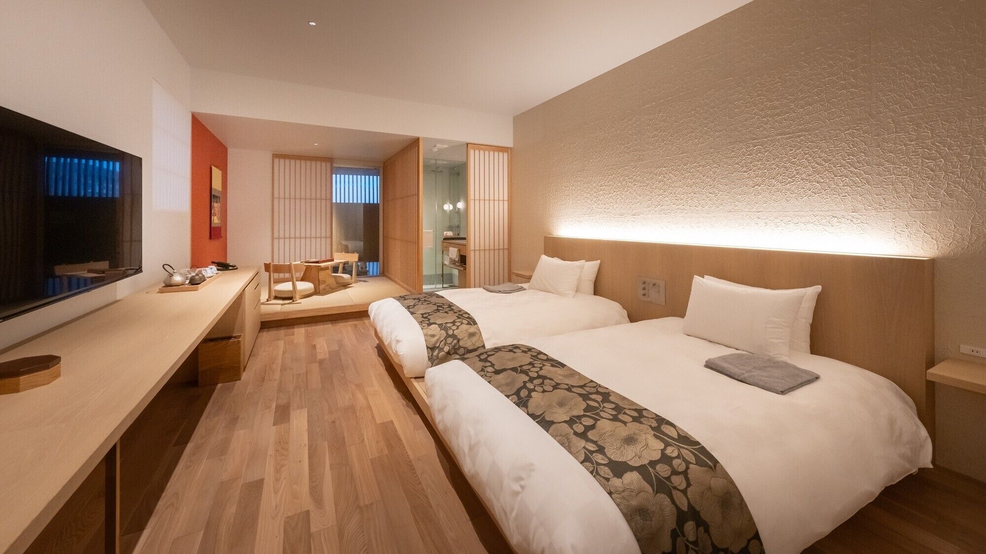 Habitació d'hotel amb dos llits, un escriptori, un televisor i una porta corredissa que dona a un bany.