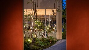 A building with large windows, a pathway leading to it, and a variety of plants and trees.