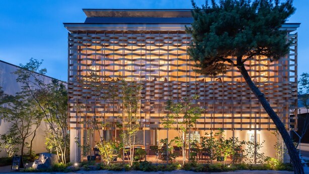 A modern building with a unique lattice facade, outdoor seating, and a well-maintained garden.
