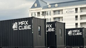 Three black shipping containers with 'Live MAX Group' and 'MAX CUBE' branding, in front of a building with 'Spa Resort LIVEMAX' signage.