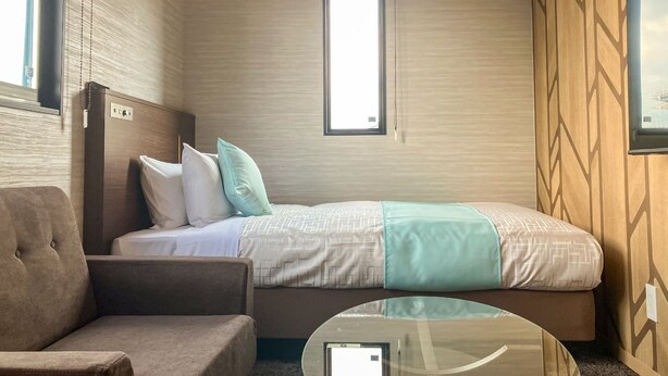 A hotel room with a bed, a chair, a glass table, and a window.