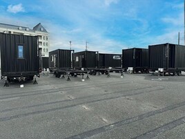 A parking lot with several black shipping containers and a building in the background.