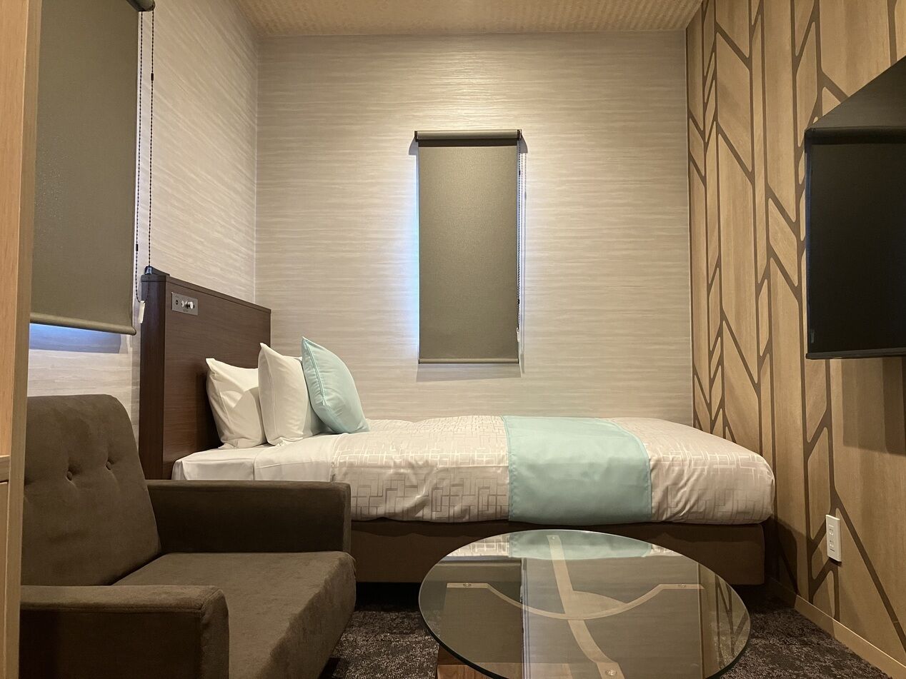 Habitación de hotel compacta con cama, sofá, mesita y televisor.