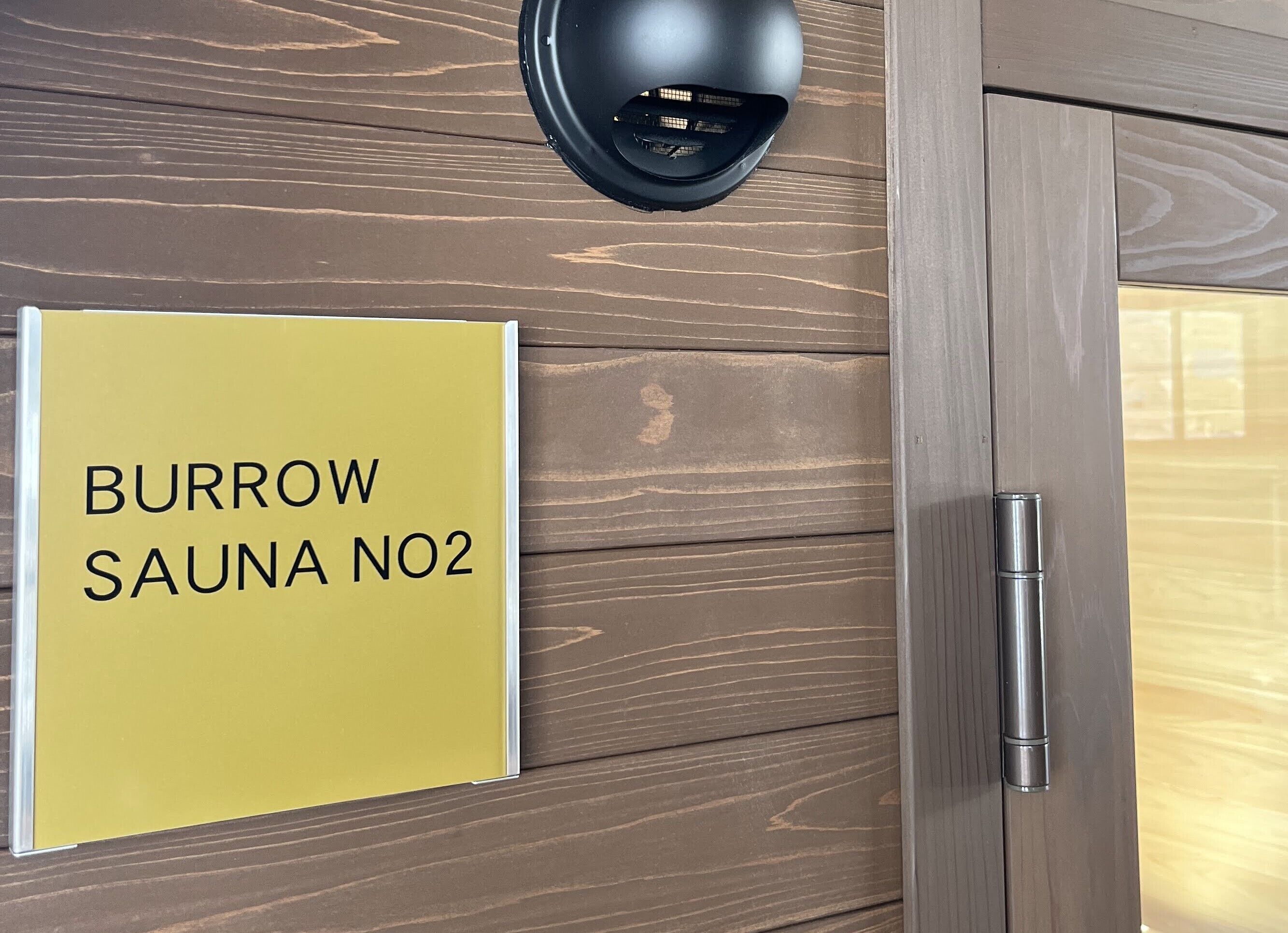 Un letrero que dice 'BURROW SAUNA NO2' sobre una pared de madera.