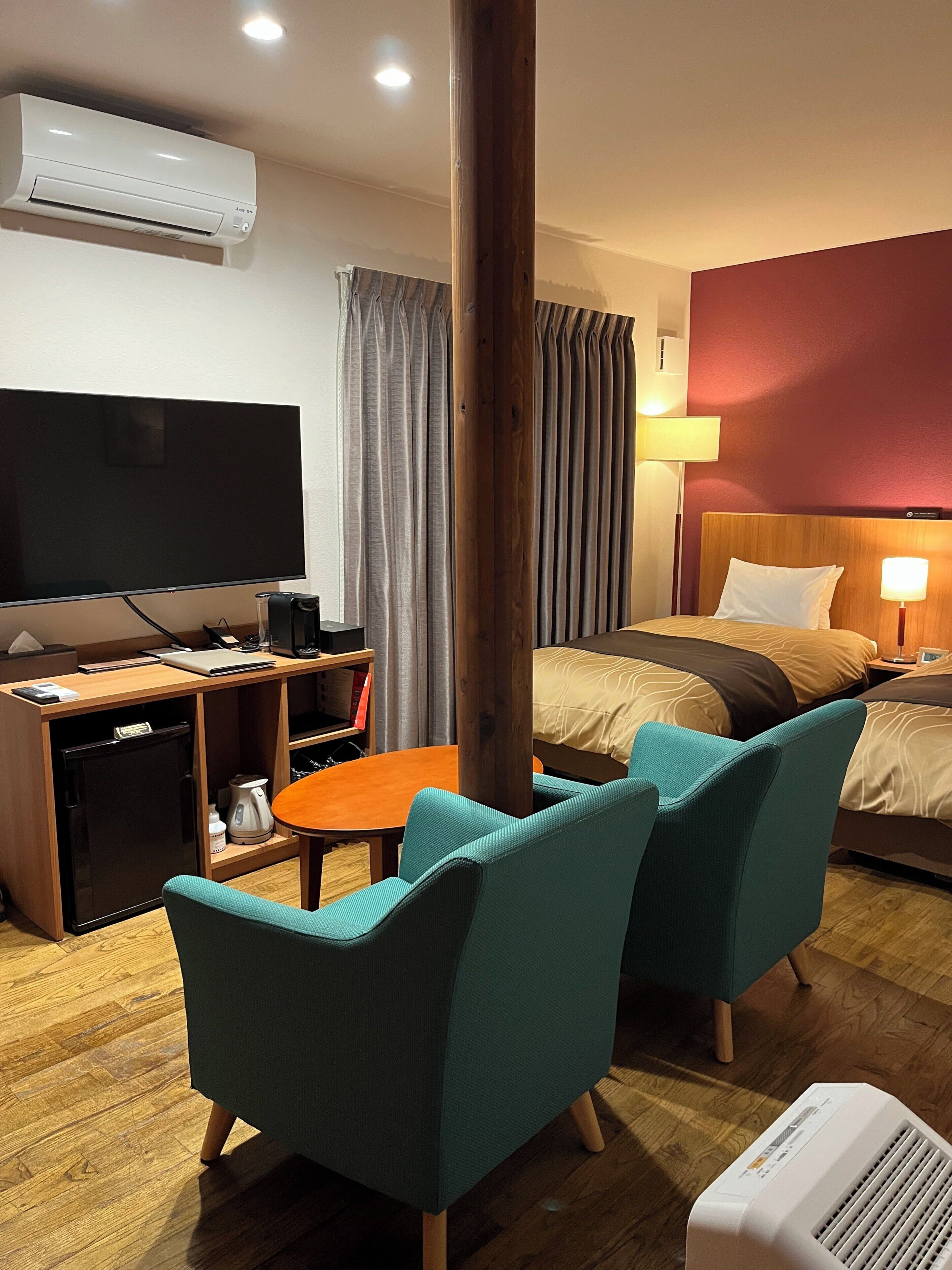 Habitación de hotel con cama, televisión, escritorio con computadora, cafetera, silla y aire acondicionado.
