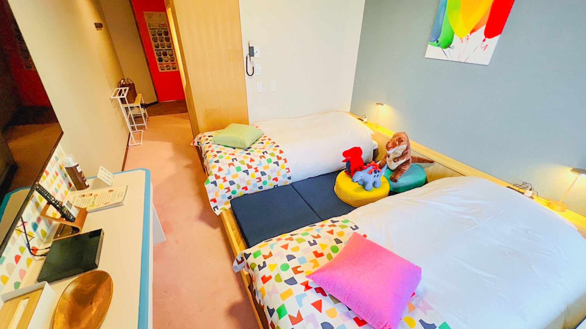 Ein Hotelzimmer mit zwei Betten, einem Schreibtisch mit Stuhl, einem Telefon und einer Wand mit einem farbenfrohen Poster.