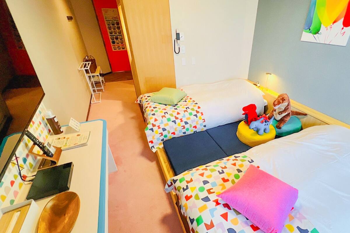 A hotel room with two beds, a desk with a chair, a telephone, and a wall with a colorful poster.