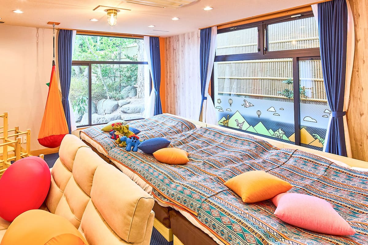 Ein Schlafzimmer mit Bett, Kissen, einem Hängekorbstuhl und einem Fenster mit Blick auf Bäume.