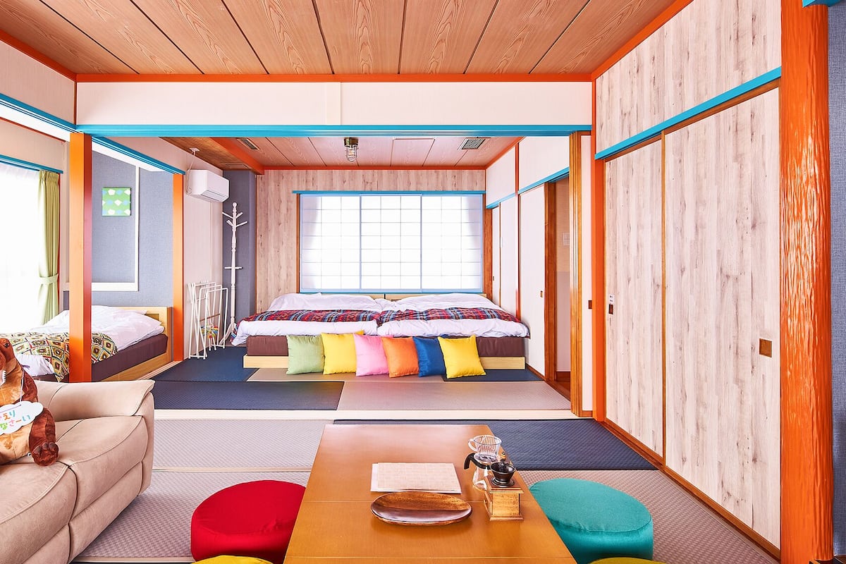Ein traditioneller japanischer Raum mit Tatami-Bodenbelag, einem Futon, einem niedrigen Holztisch und einer Couch mit Kissen.