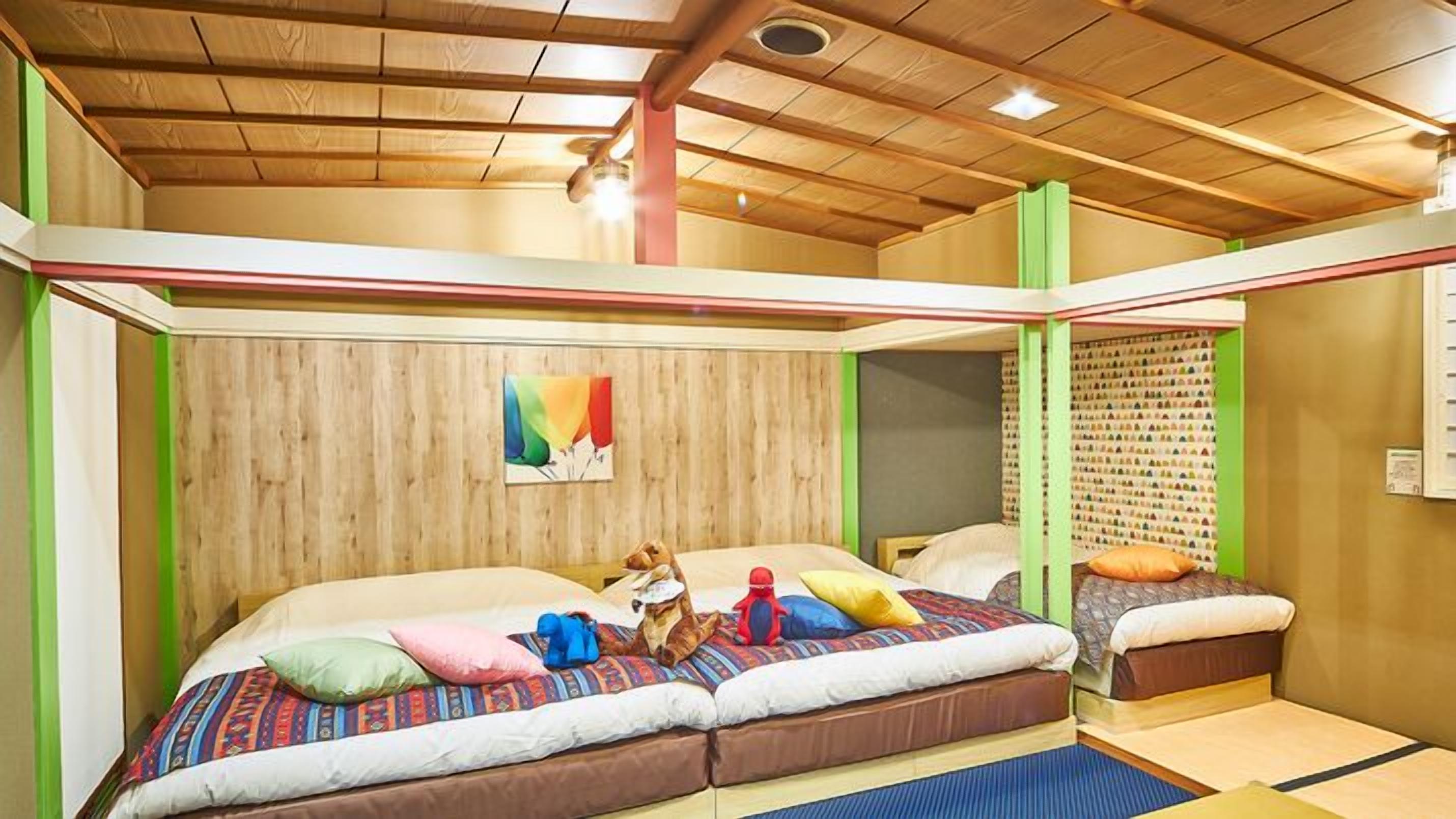 Ein Zimmer mit Holzbalkendecke, zwei Betten mit bunter Bettwäsche, einem kleinen Hund und einer Wand mit einem farbenfrohen Gemälde.