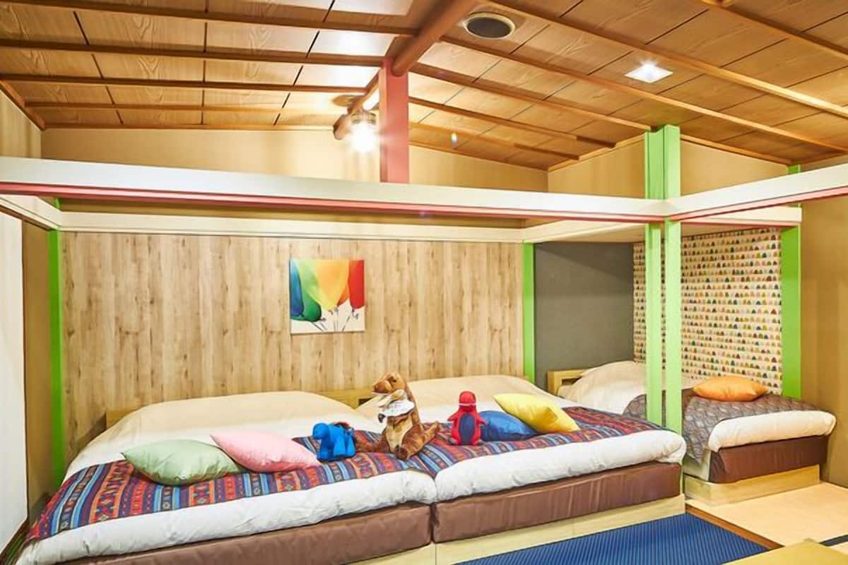 Ein Zimmer mit Holzbalkendecke, zwei Betten mit bunter Bettwäsche, einem kleinen Hund und einer Wand mit einem farbenfrohen Gemälde.
