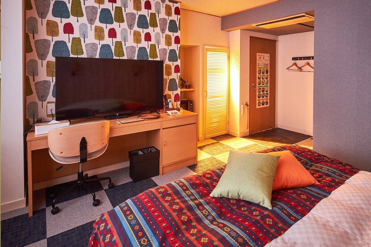 A hotel room with a bed, desk, chair, TV, and a patterned wall.