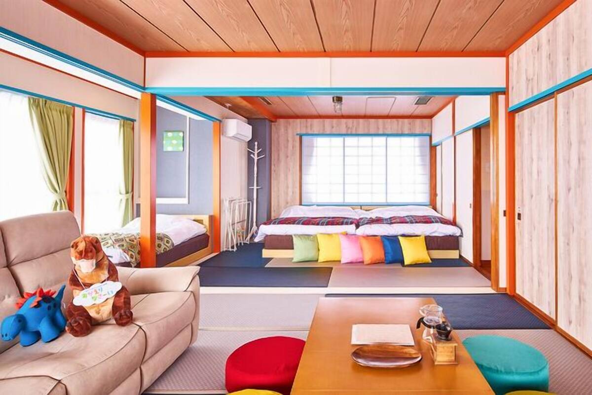 A room with a bed, a sofa, a table with items, and a window.