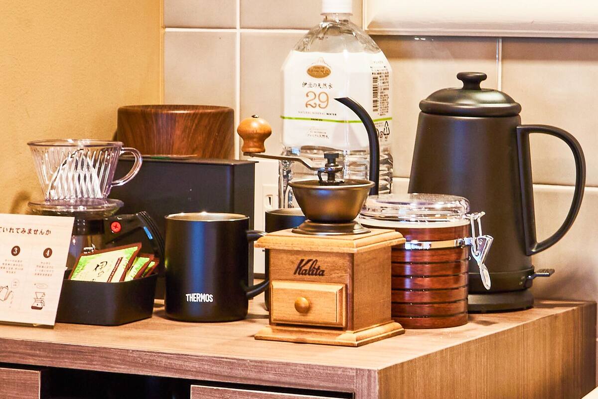 A coffee station with a coffee maker, thermos, kettle, and a bottle of water.