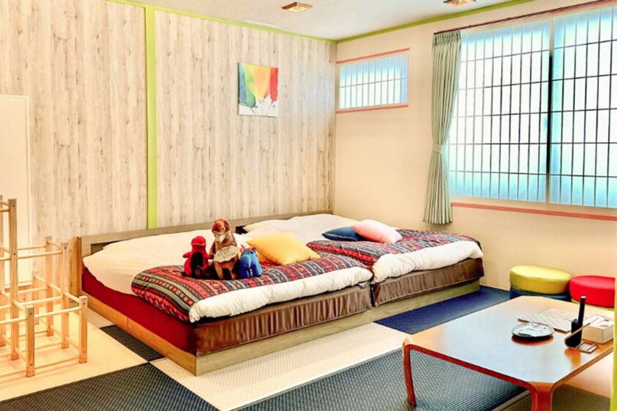 A room with two beds, a desk, a chair, a window with a view, and a wooden wall.