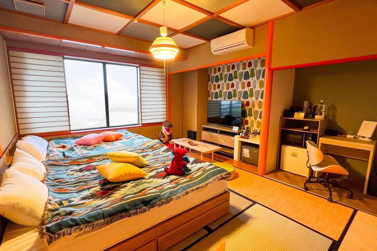 A bedroom with a bed, a desk, a chair, a TV, and an air conditioning unit.