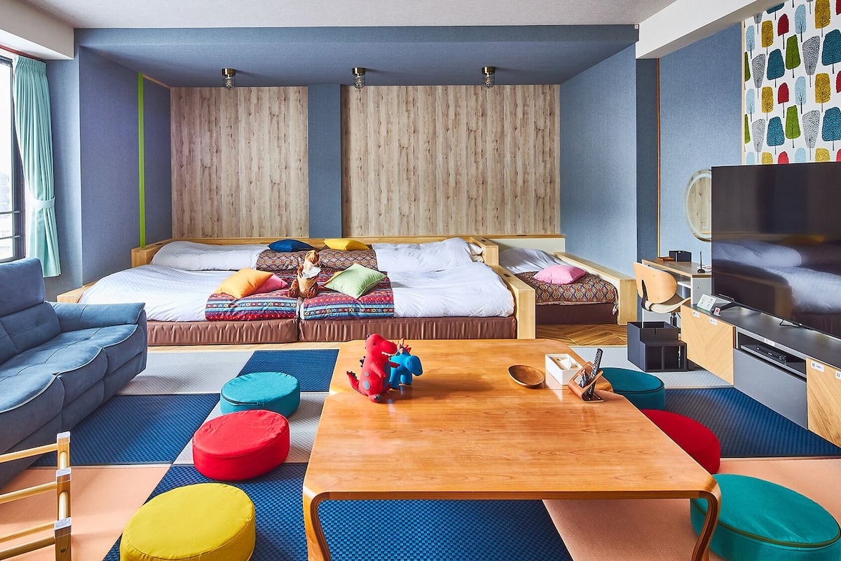 Ein modernes Zimmer mit einer Couch, einem Bett mit bunter Bettwäsche, einem Holztisch und einem Fernseher.