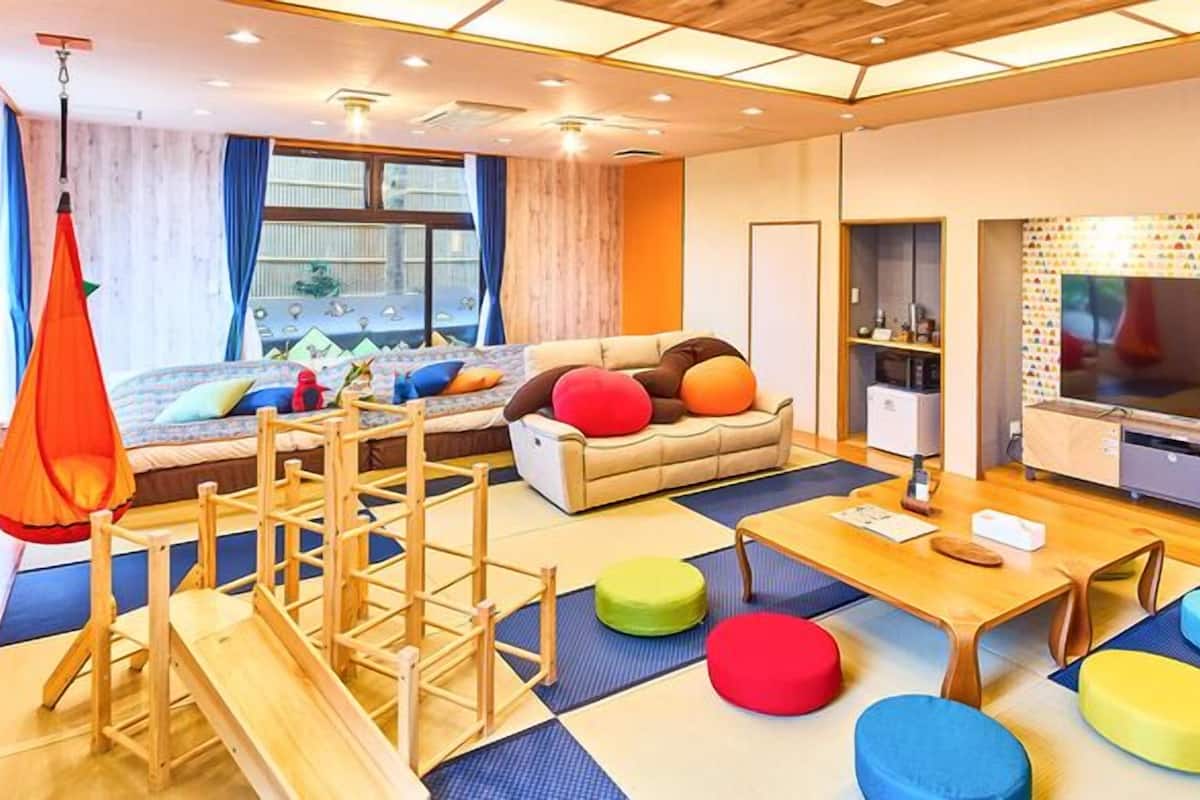 Ein modernes Wohnzimmer mit einer Couch, bunten Kissen, einem Fernseher und einer Holz-Spielstruktur.